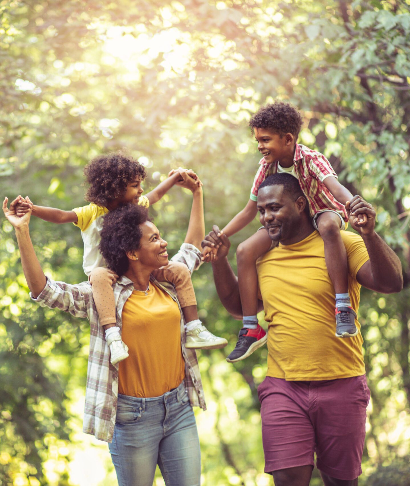 African American family walking trough park. Parents carrying children on piggyback.